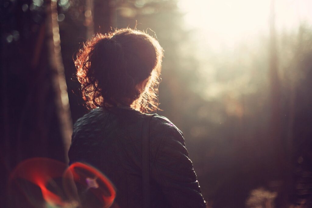 A solitary person sitting quietly in soft natural light, appearing physically present but emotionally distant, reflecting stillness, fatigue, and inner awareness.
