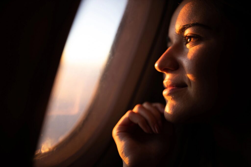 Close up of smiling woman looking at sunset through airplane window.